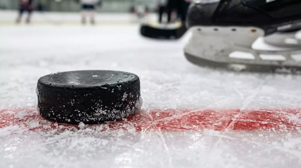 Nahaufnahme eines schwarzen Eishockey-Pucks auf der weißen Eisfläche vor einem Schlittschuh