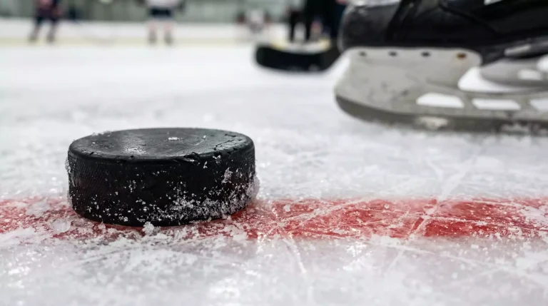 Nahaufnahme eines schwarzen Eishockey-Pucks auf der weißen Eisfläche vor einem Schlittschuh